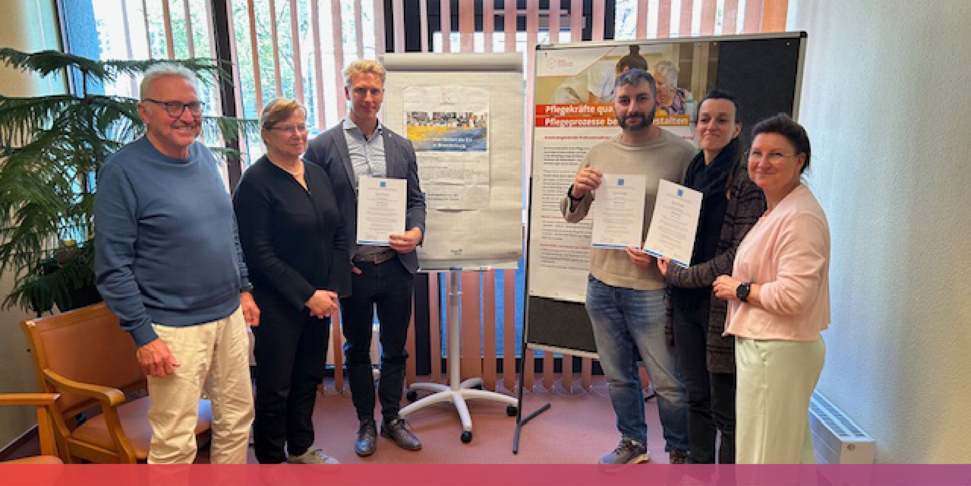 Etliche Menschen stehen vor einer Metaplanwand und einem Flipchart, drei von ihnen halten Urkunden in den Händen.