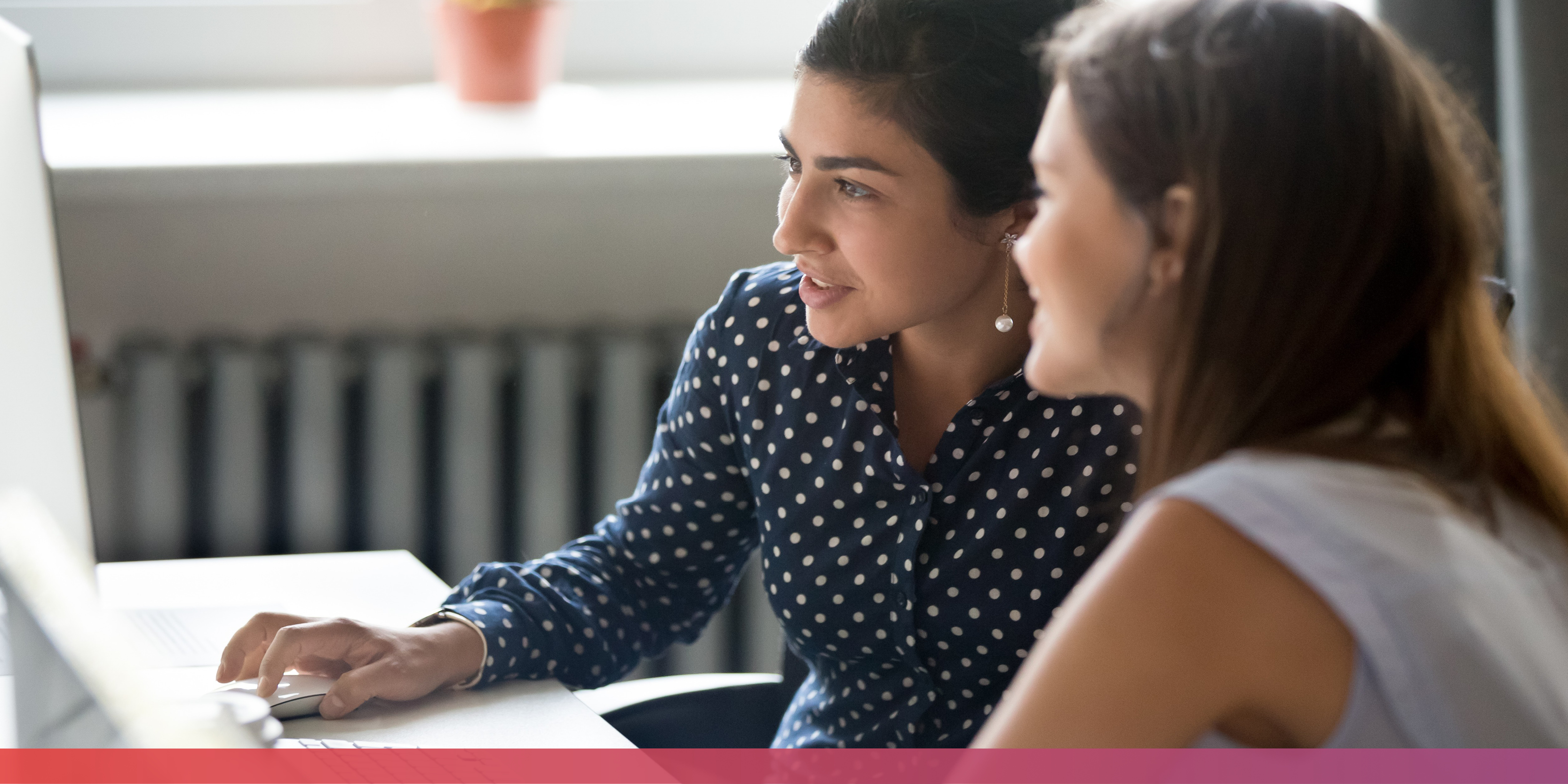 Zwei junge Frauen sitzen gemeinsam vor einem PC-Monitor und arbeiten gemeinsam an etwas.