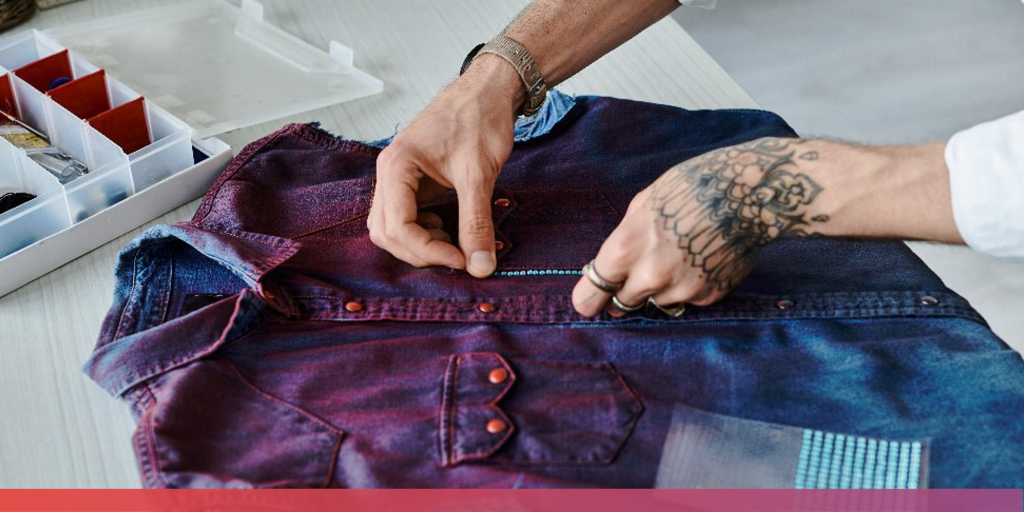 Nahaufnahme zweier Hände, die ein Jeanshemd gestalte; im Hintergrund Nähutensilien.