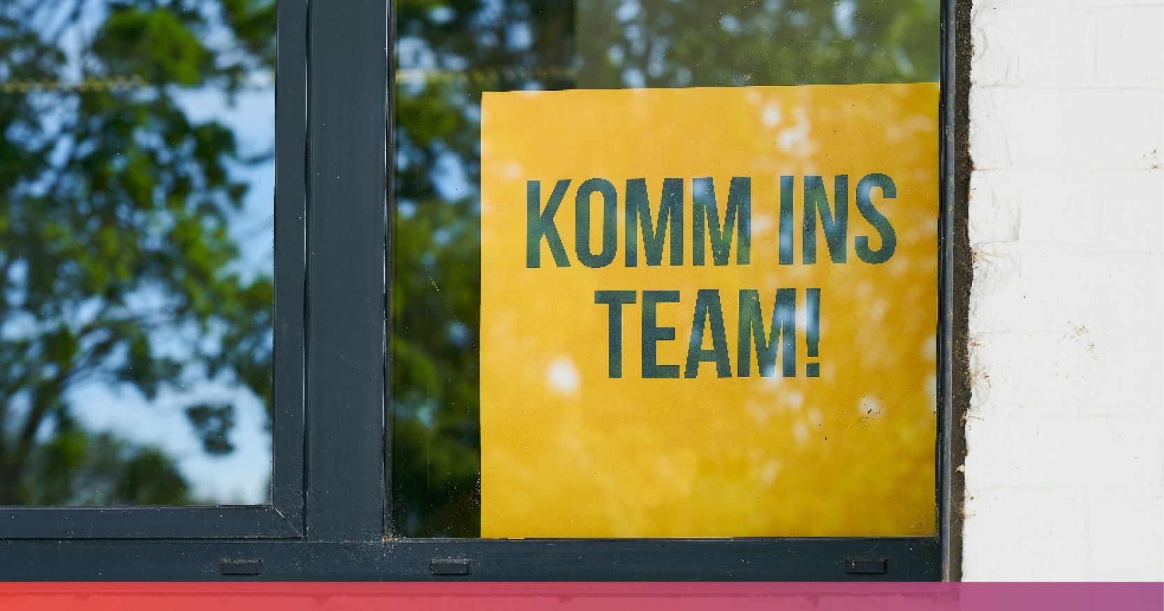 Eine Fensterscheibe hinter der ein Schild zu sehen ist mit der Aufschrifft: Komm ins Team!