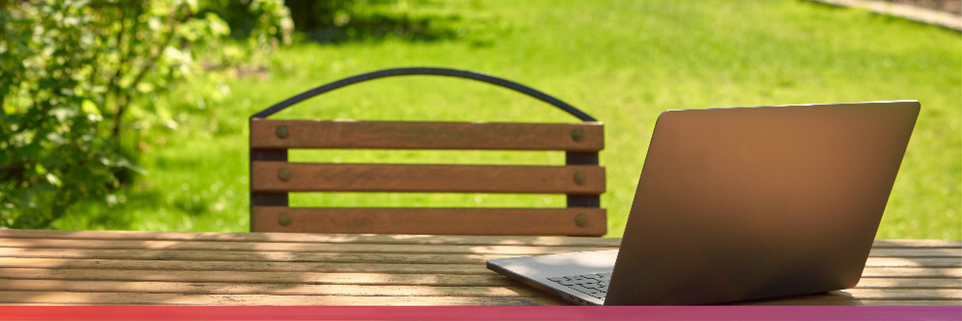 Ein Gartentisch auf dem ein aufgeklappter Laptop steht, im Hintergrund eine große Rasenfläche.