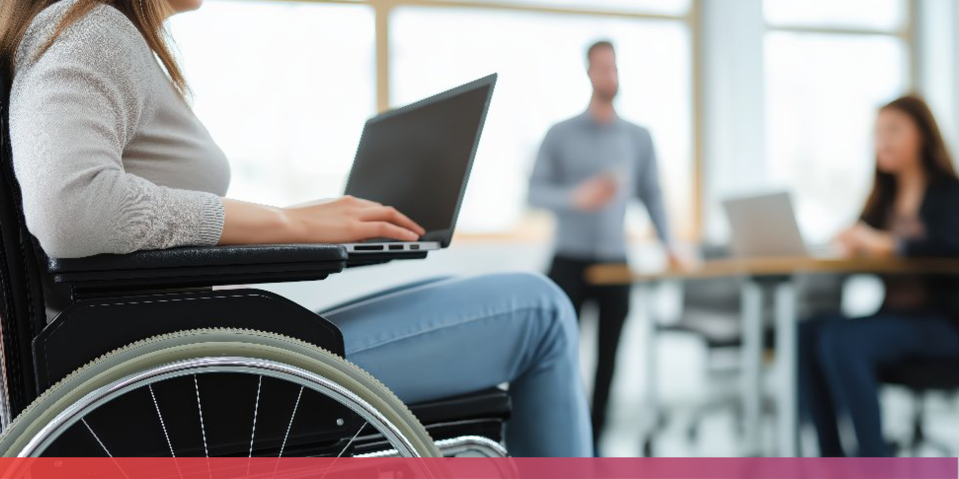 Eine Frau im Rollstuhl mit Laptop auf dem Schoß im Vordergrund, im Hintergrund ein stehender Mann und eine Frau, die an einem Tisch sitzt, auf dem ebenfalls ein Laptop steht.