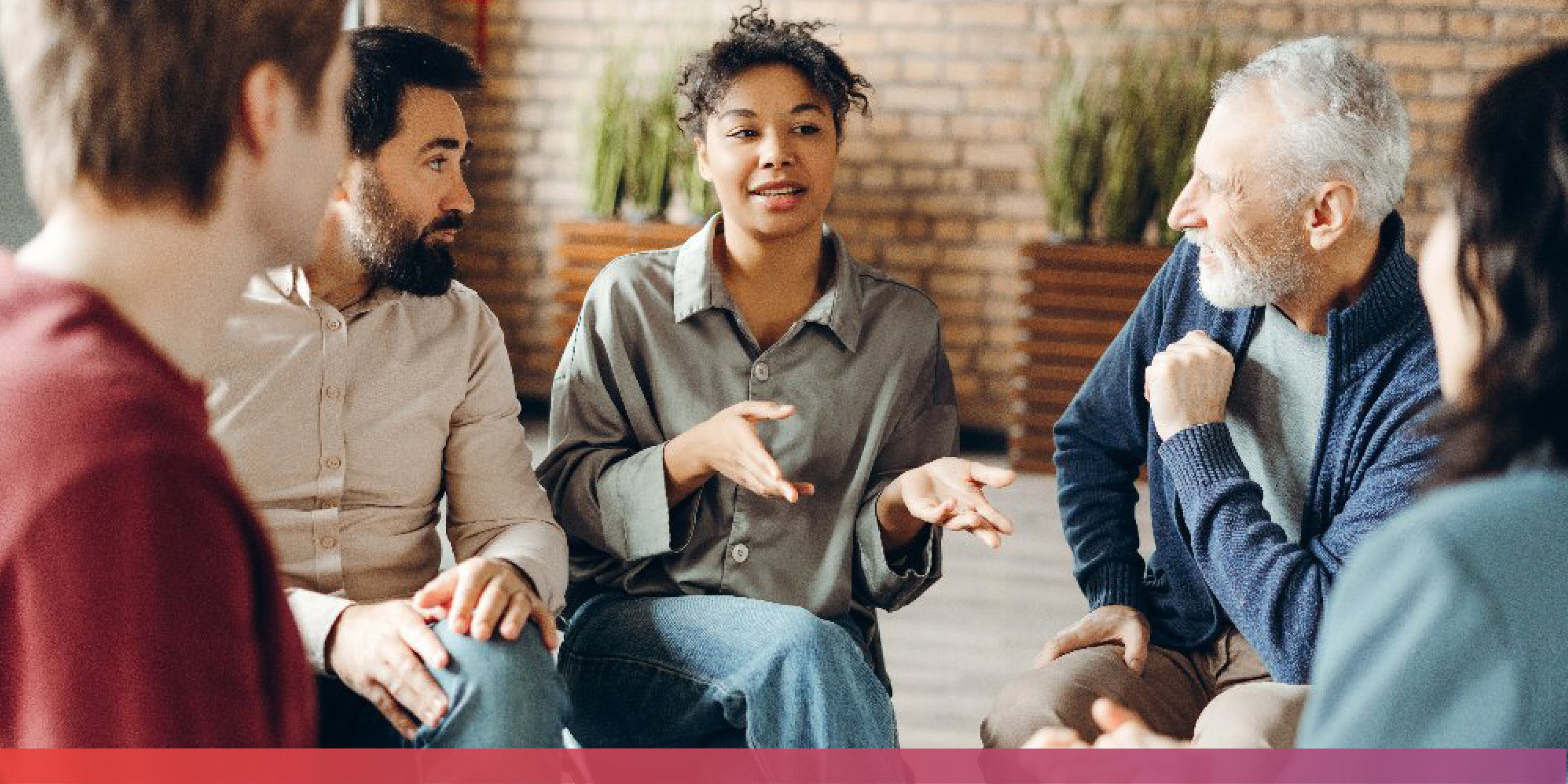 Mehrere Menschen sitzen um eine junge Frau in einem Stuhlreis wie im Rahmen einer Gruppentherapie.