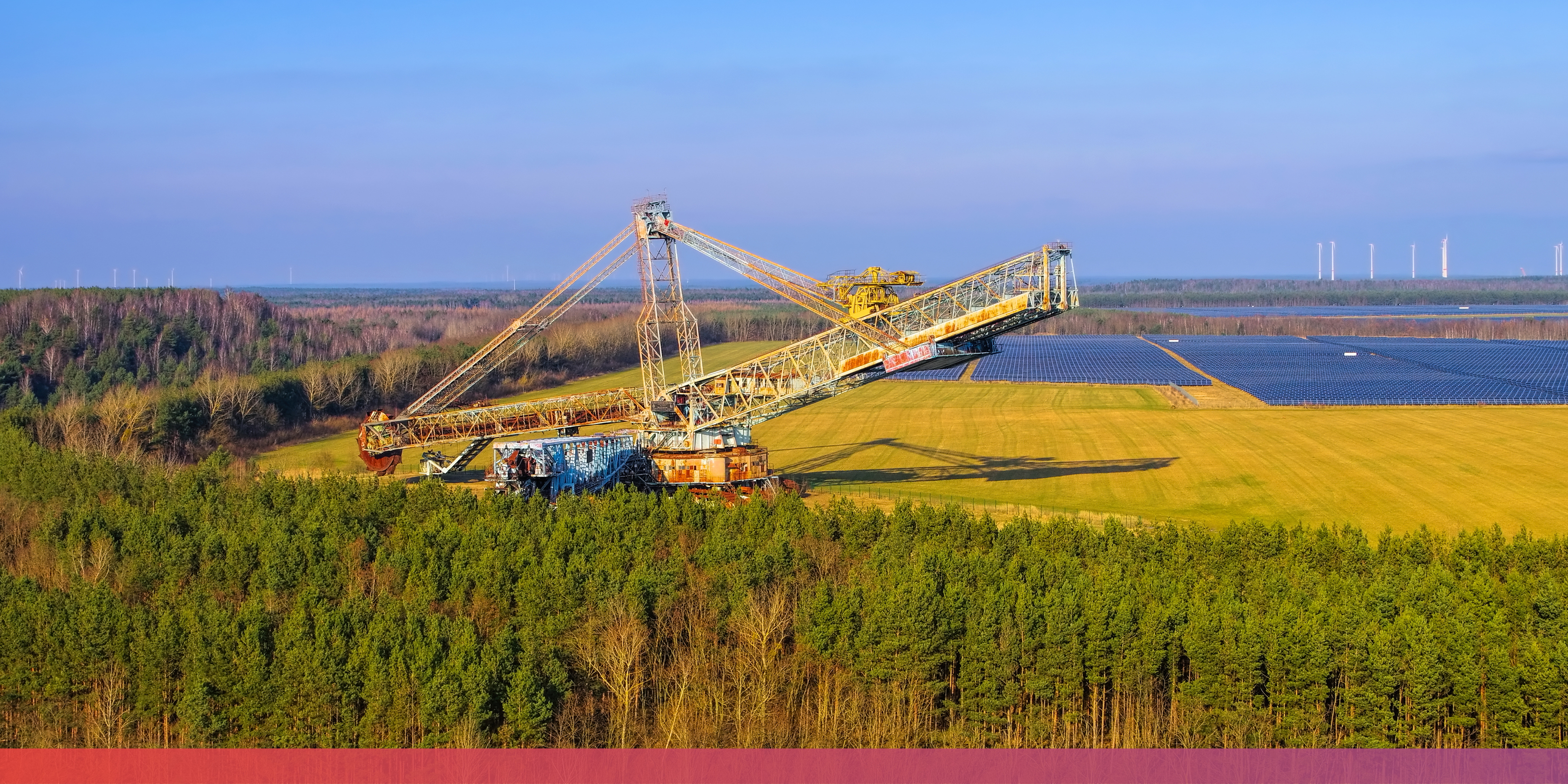 Ehemaliger Tagebau mit riesigem Bagger; im Hintergrund eine große Fläche mit PV-Anlagen und Windräder.