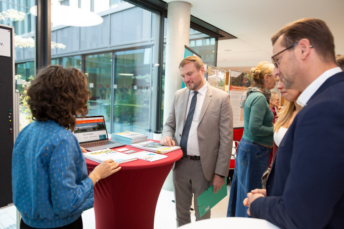 Minister Daniel Keller steht an einem Stehtisch und blickt auf das darauf liegende Ansichtsmaterial. Ihm zugewandt und von hinten sichtbar eine Frau, rechts neben ihm ILB-Vorstand Christian Kistner.